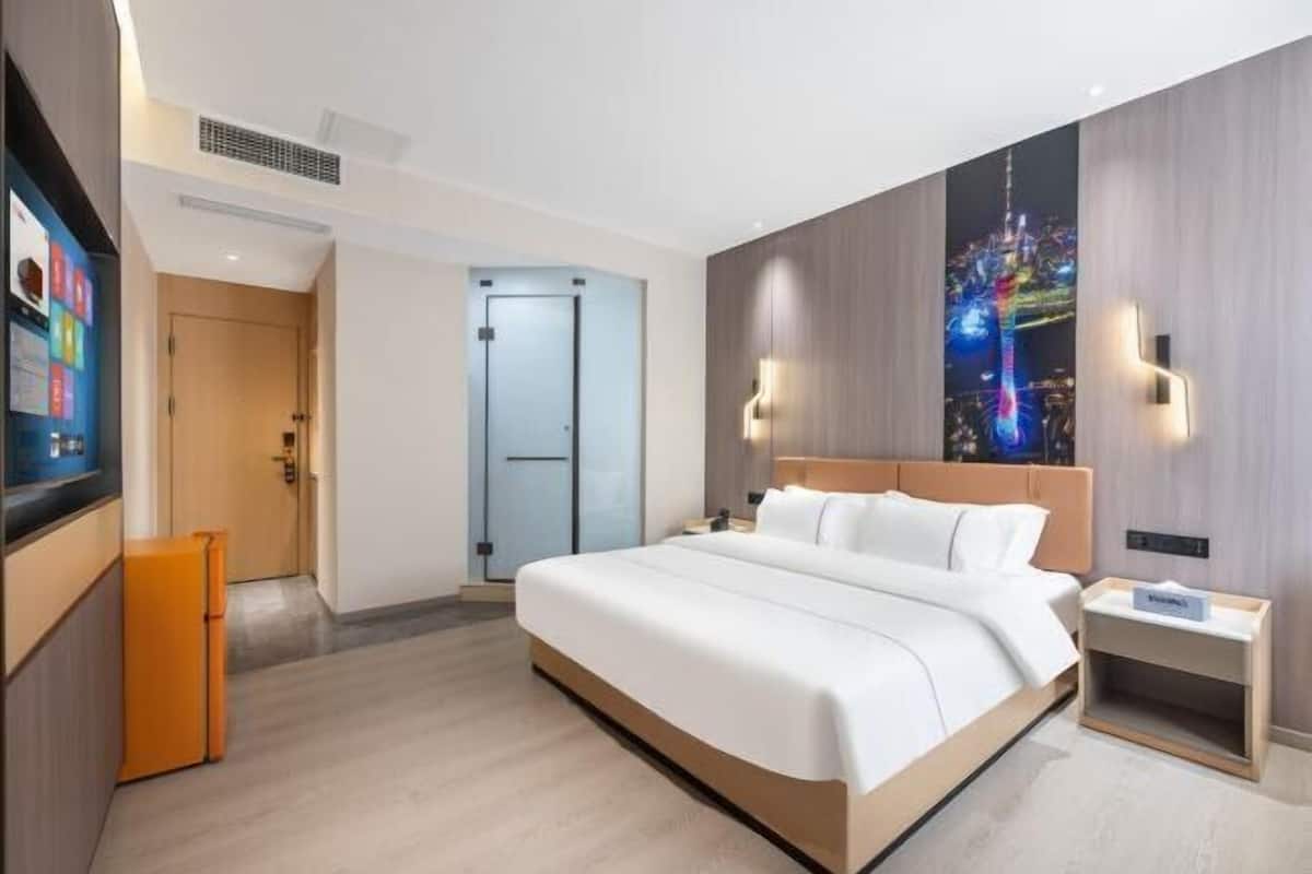 A modern hotel room with a large bed, a television, a refrigerator, and a cityscape mural on the wall.