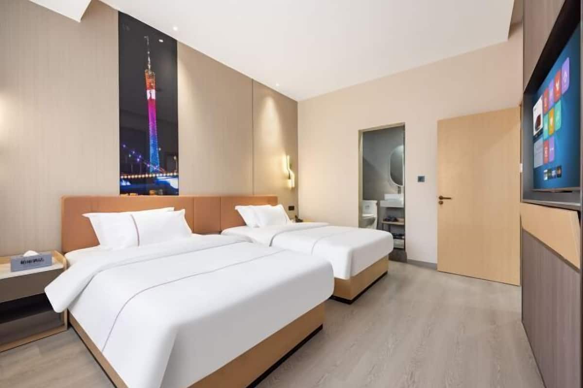 A hotel room with two beds, a large window with a cityscape view, a flat-screen TV, and a wooden door.