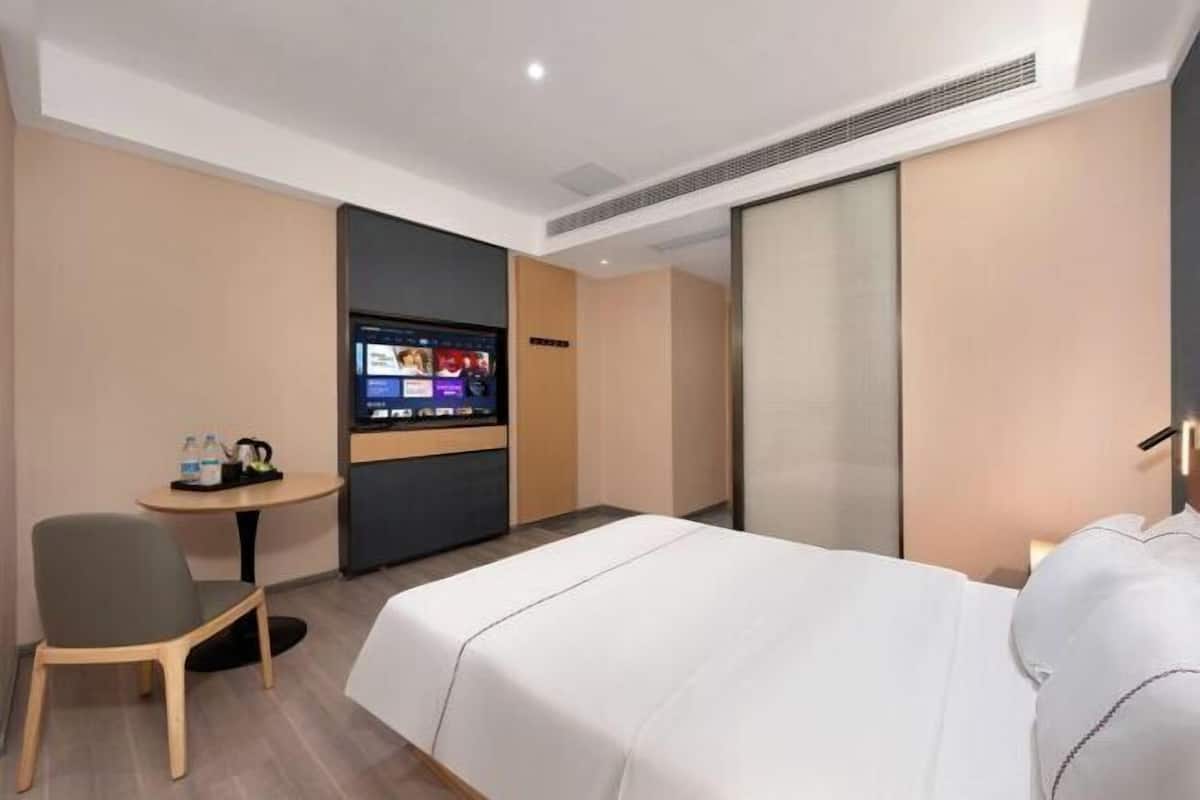 A hotel room with a bed, a desk, a chair, a TV, and a minibar.