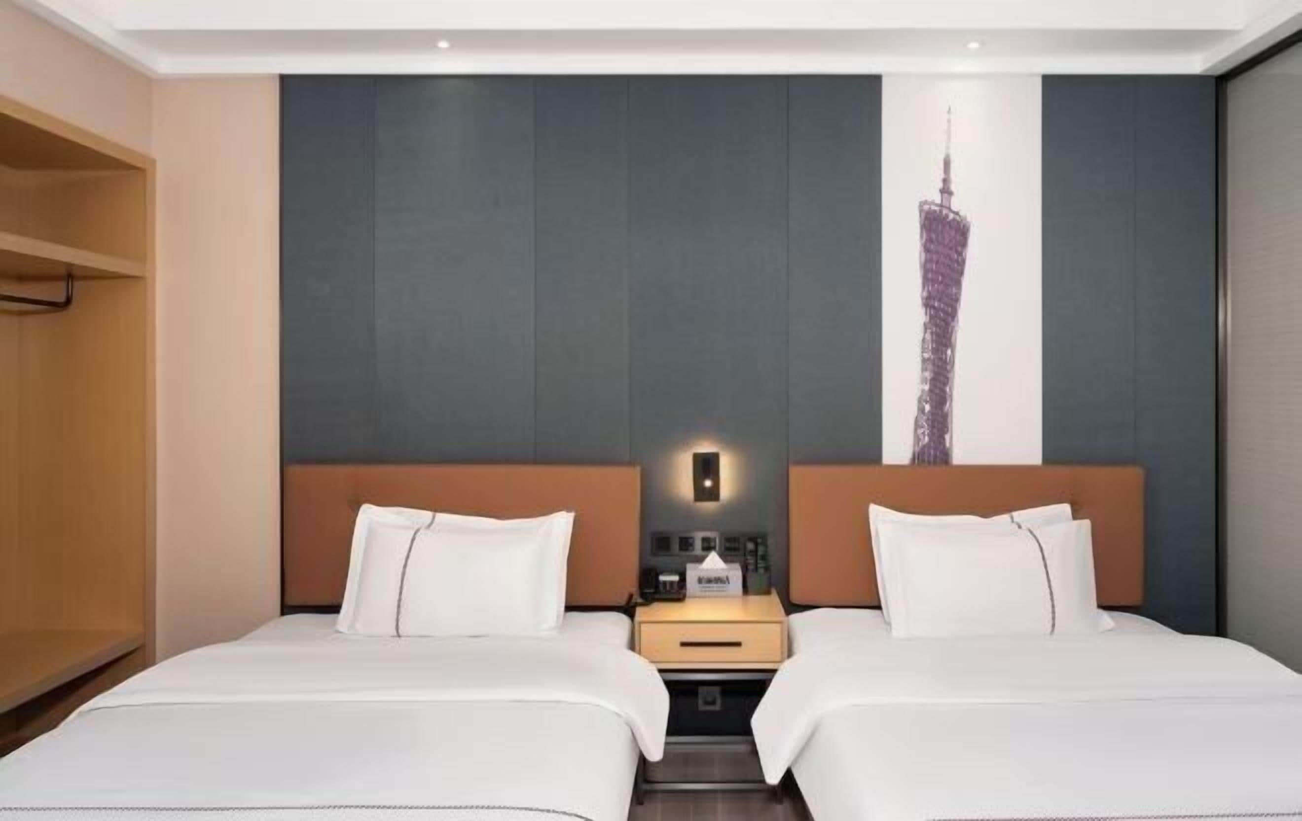 A hotel room with two beds, a nightstand, a wall-mounted light, and a large cityscape painting.
