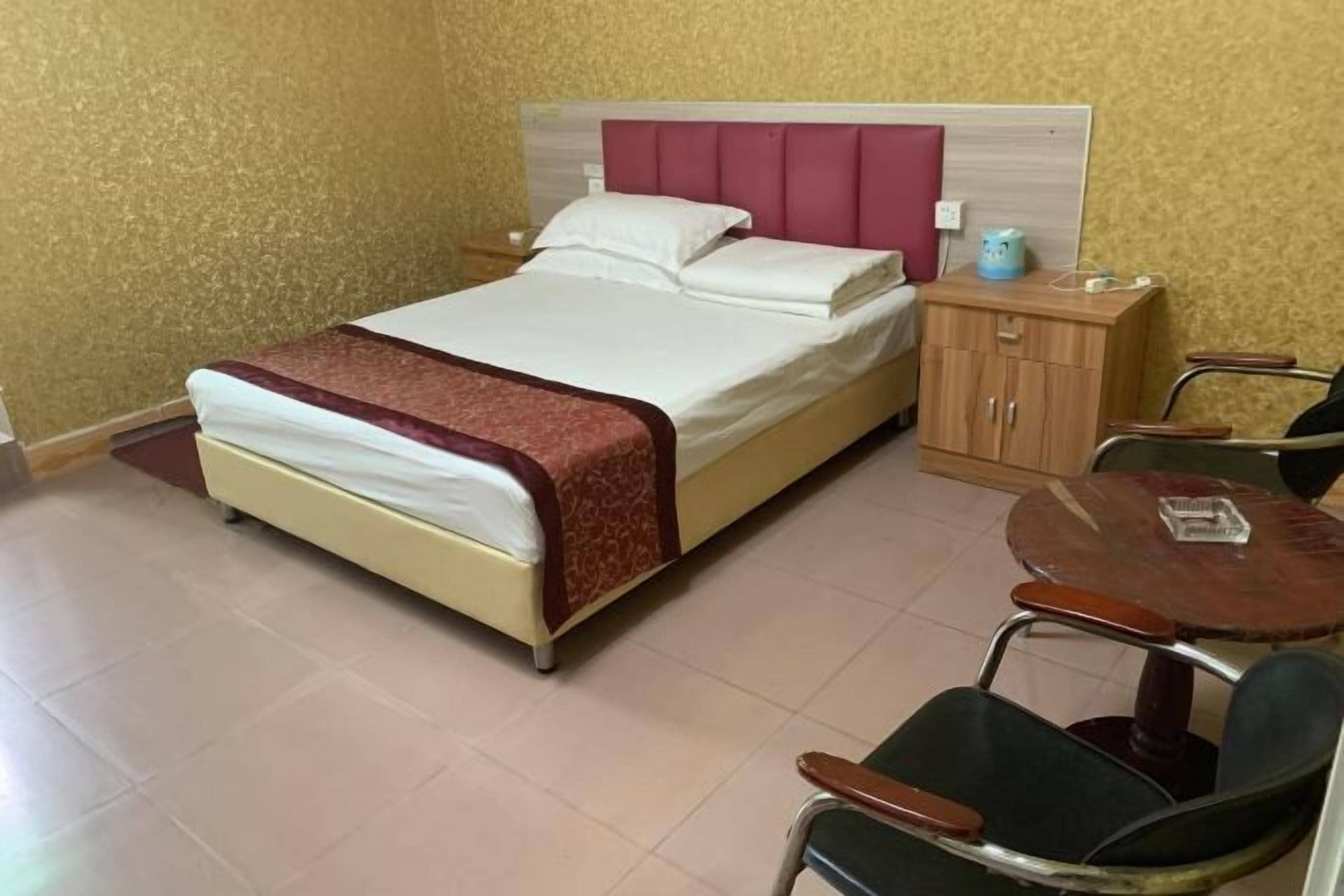 Una habitación de hotel con una cama, un pequeño aparador de madera, una mesa y dos sillas.