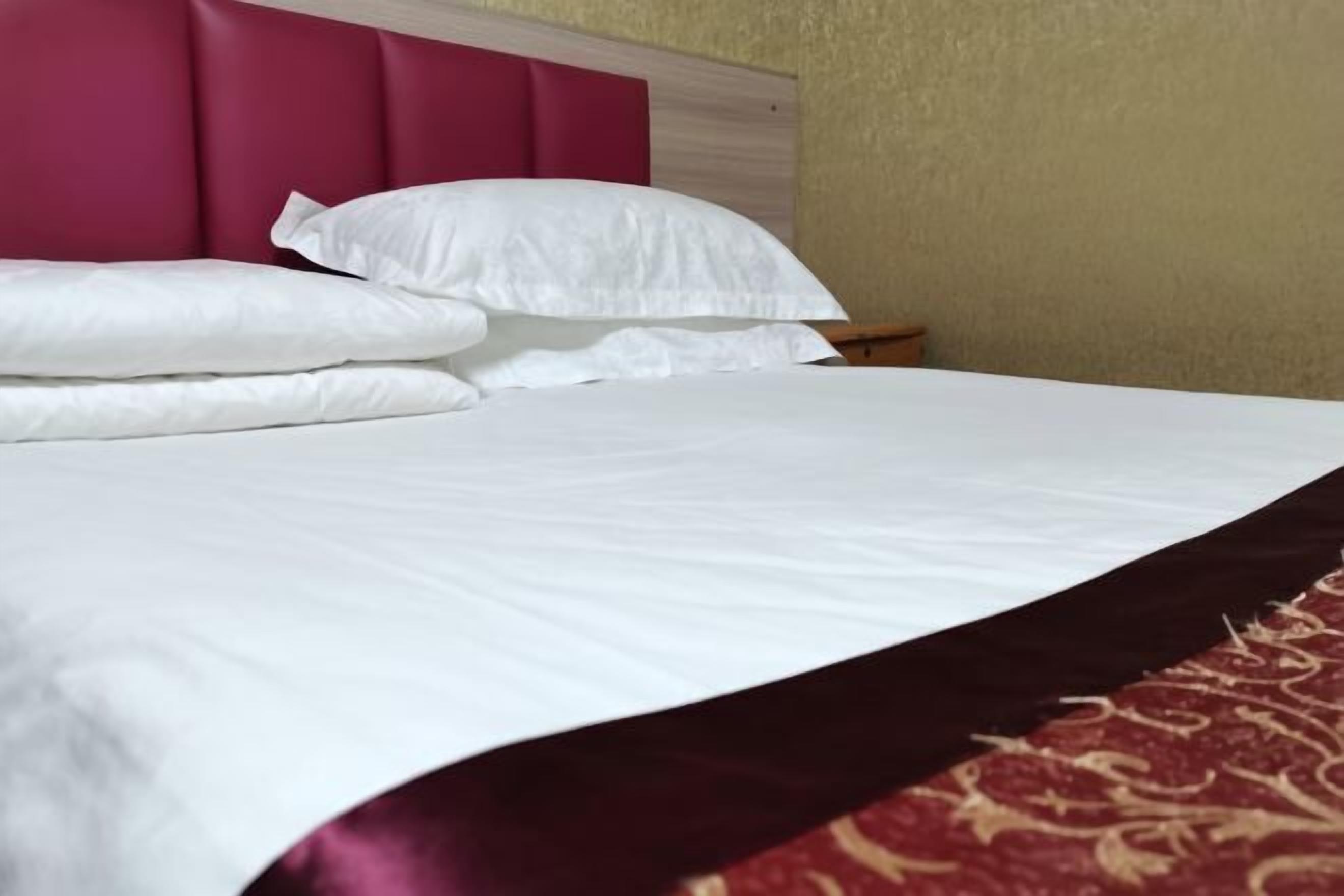 Een bed met witte lakens en een rood hoofdeinde.