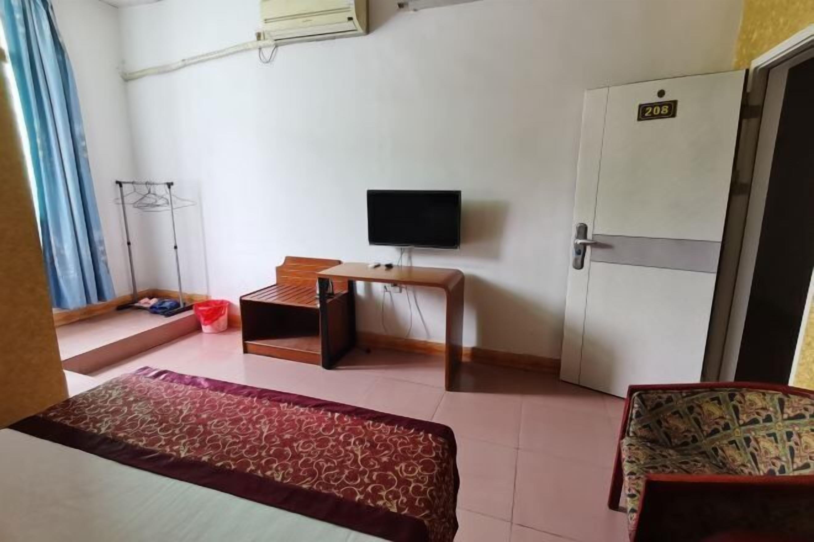 A hotel room with a bed, a TV, a desk, a wardrobe, and a window with curtains.