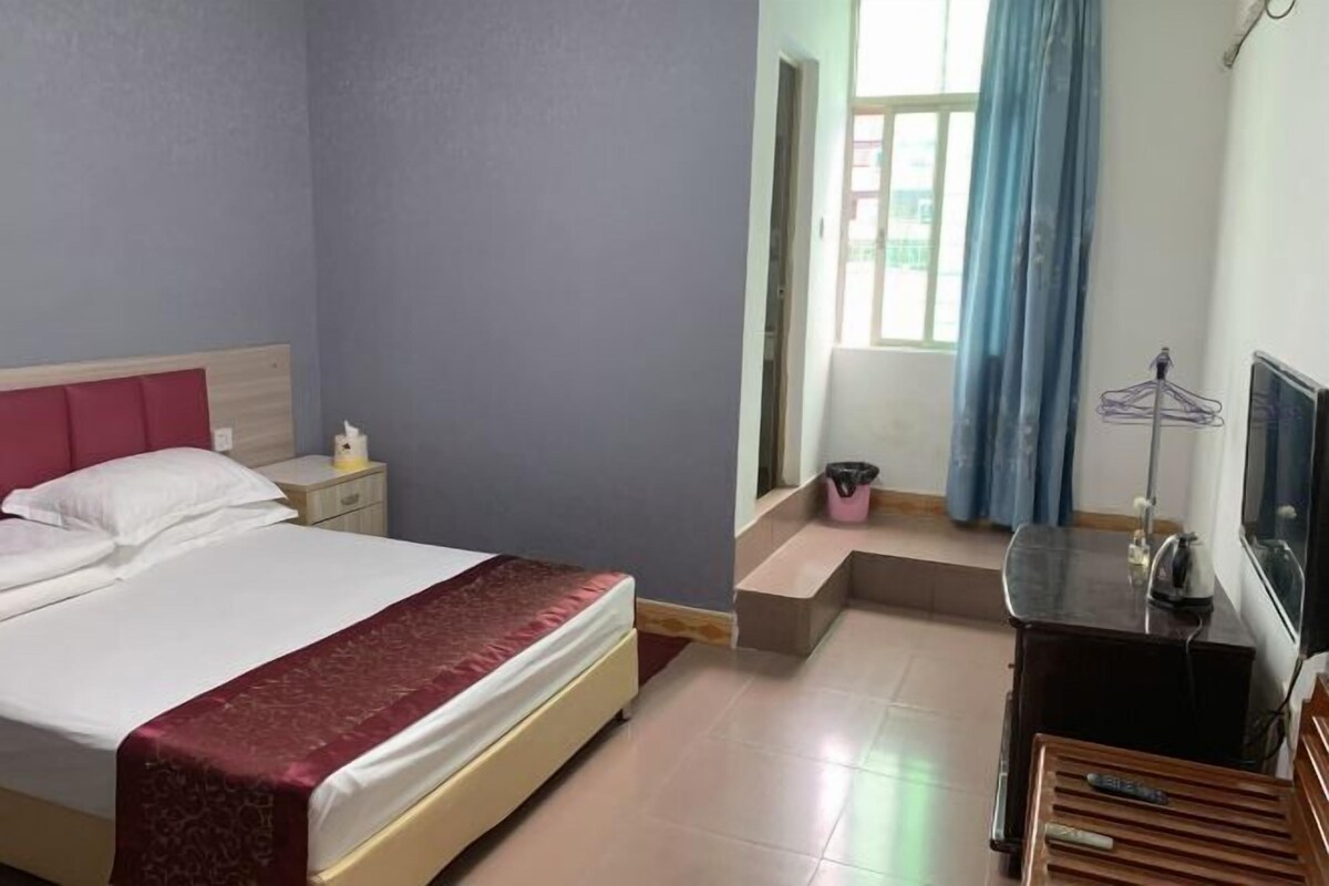 A hotel room with a bed, a nightstand, a desk, a TV, and a window with curtains.