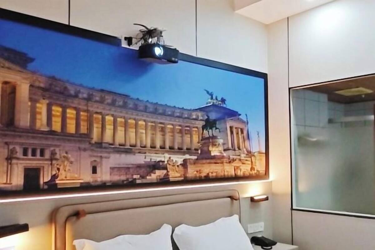 A hotel room with a large bed, a flat-screen TV mounted on the wall, and a window with frosted glass.