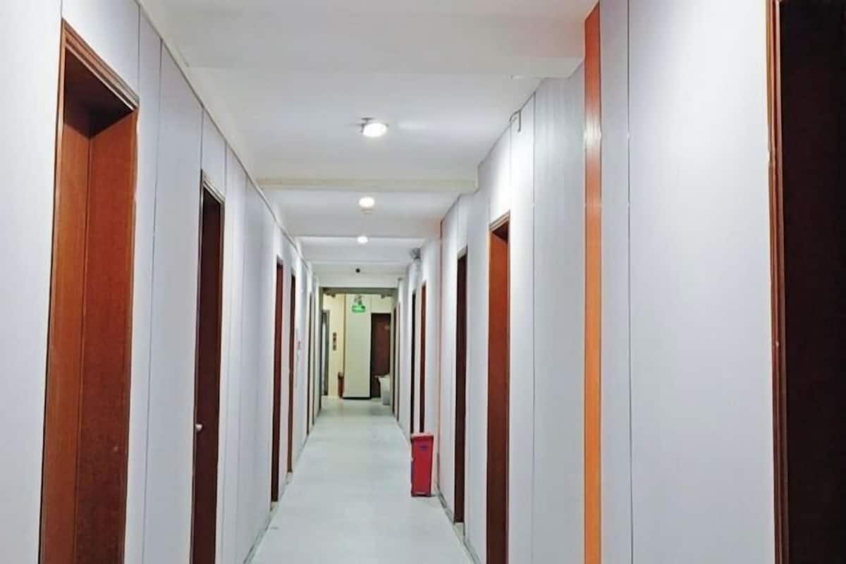 A long, narrow hotel corridor with doors on both sides, a trash bin in the center, and a ceiling light.