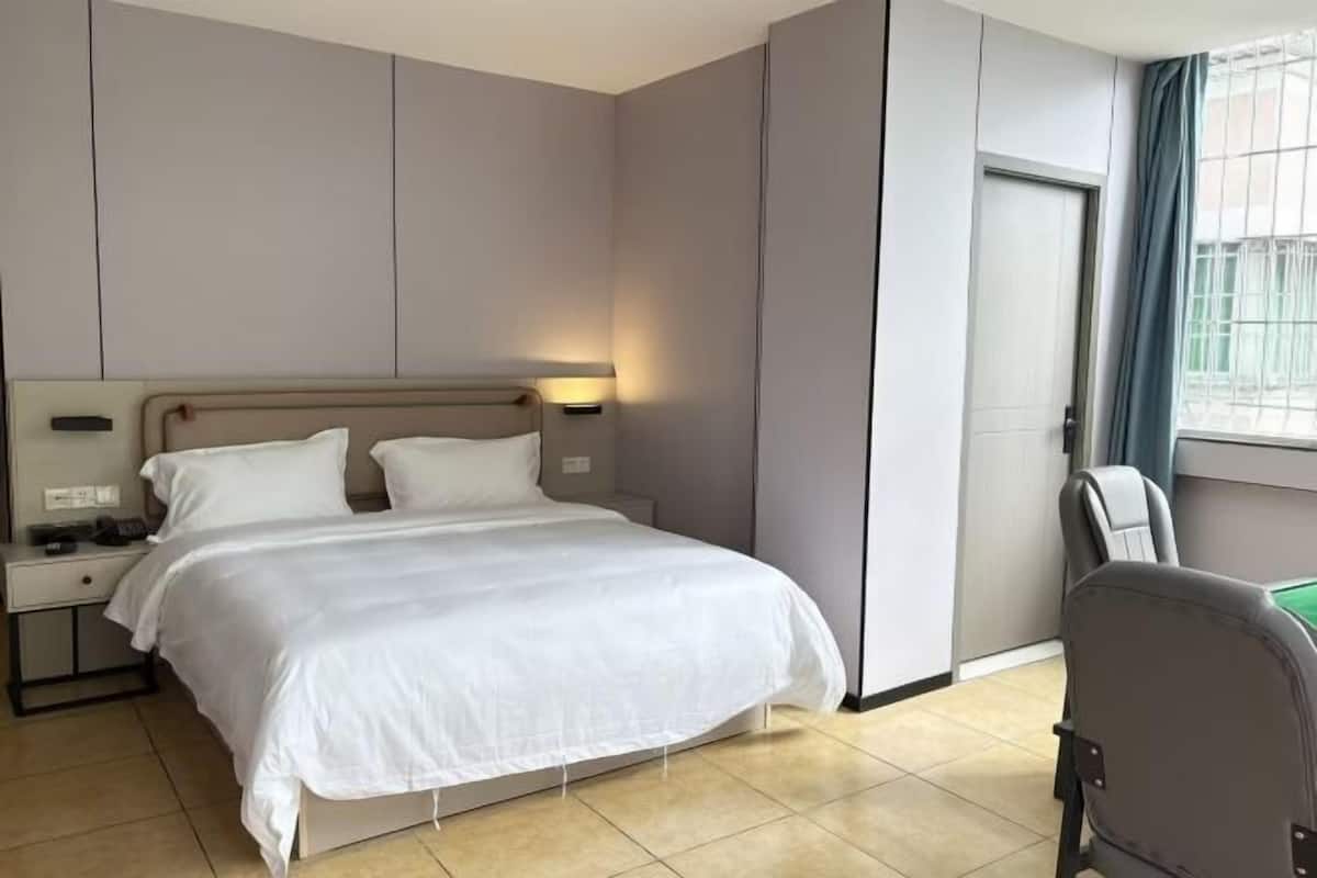 A hotel room with a bed, bedside table, lamp, chair, and a window with curtains.