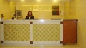 A reception desk with a receptionist, a clock, and a digital display. - Dexin Hotel Taishan (Taishan)