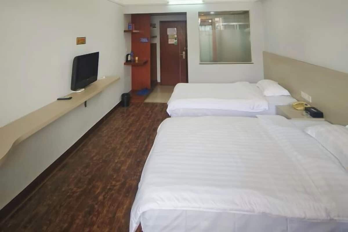 A hotel room with two beds, a television on a shelf, a door, and a window.