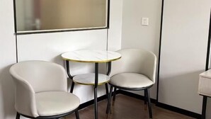 A corner of a room with two white chairs and a small round table with a gold rim. - Dexin Hotel Taishan (Taishan)