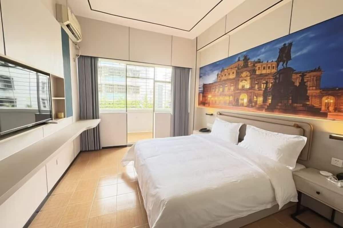 A hotel room with a bed, a TV, a painting, and a window.