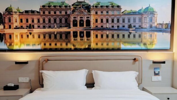 A hotel room with a large bed, two bedside tables, and a wall-mounted painting of a building. - Dexin Hotel Taishan (Taishan)