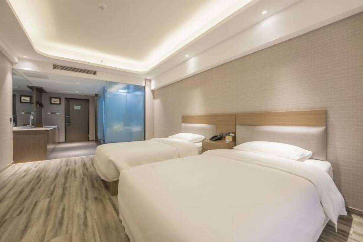 Habitación de hotel con dos camas, una mesita de noche con un teléfono, un espejo y un baño visible a través de una puerta abierta.
