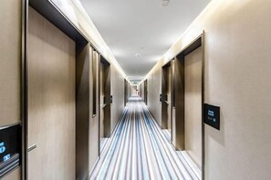 A hotel hallway with striped carpet, doors on both sides, and a digital sign on the right wall. - Midland Marriott Hotel (West Coast New Area City Balcony Branch) (Qingdao)