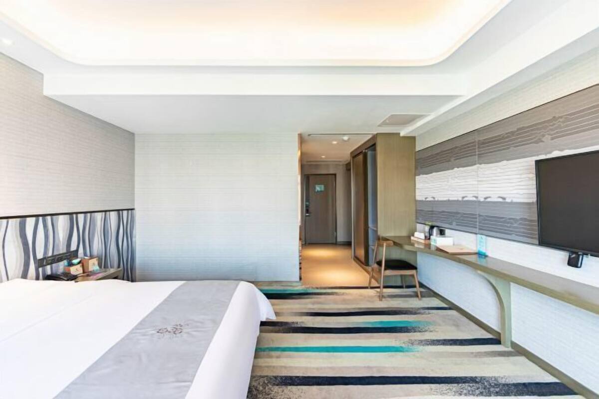 Habitación de hotel moderna con cama, escritorio, televisor de pantalla plana y vista a la ciudad.