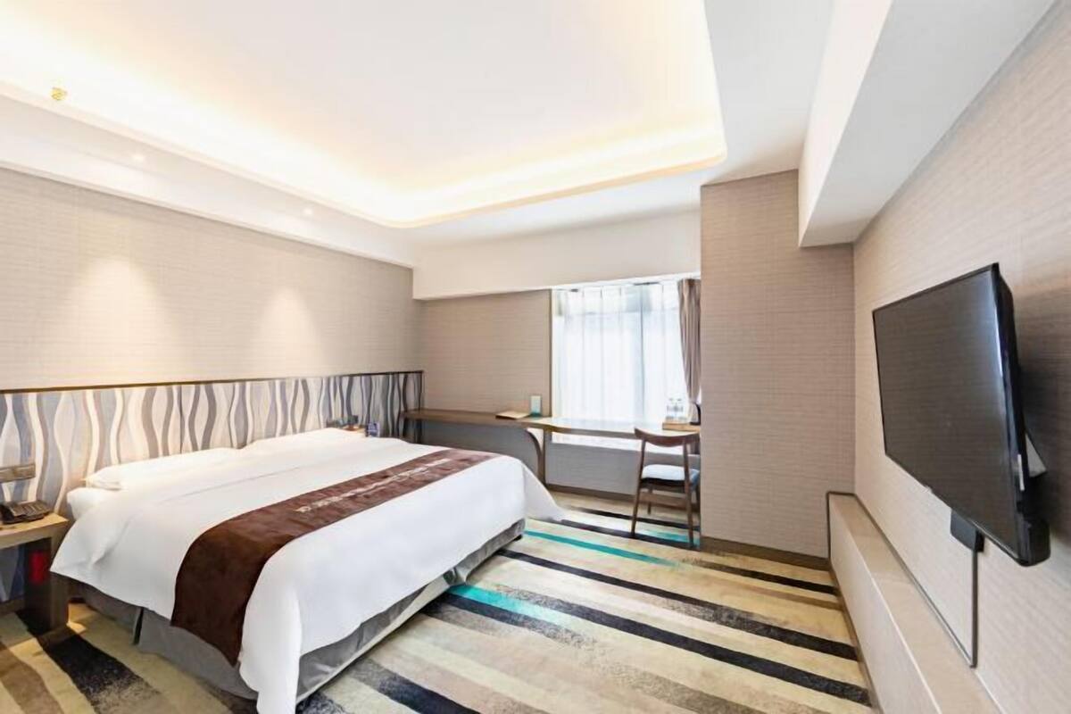 Una habitación de hotel con cama, escritorio, silla, televisor y ventana con cortinas.