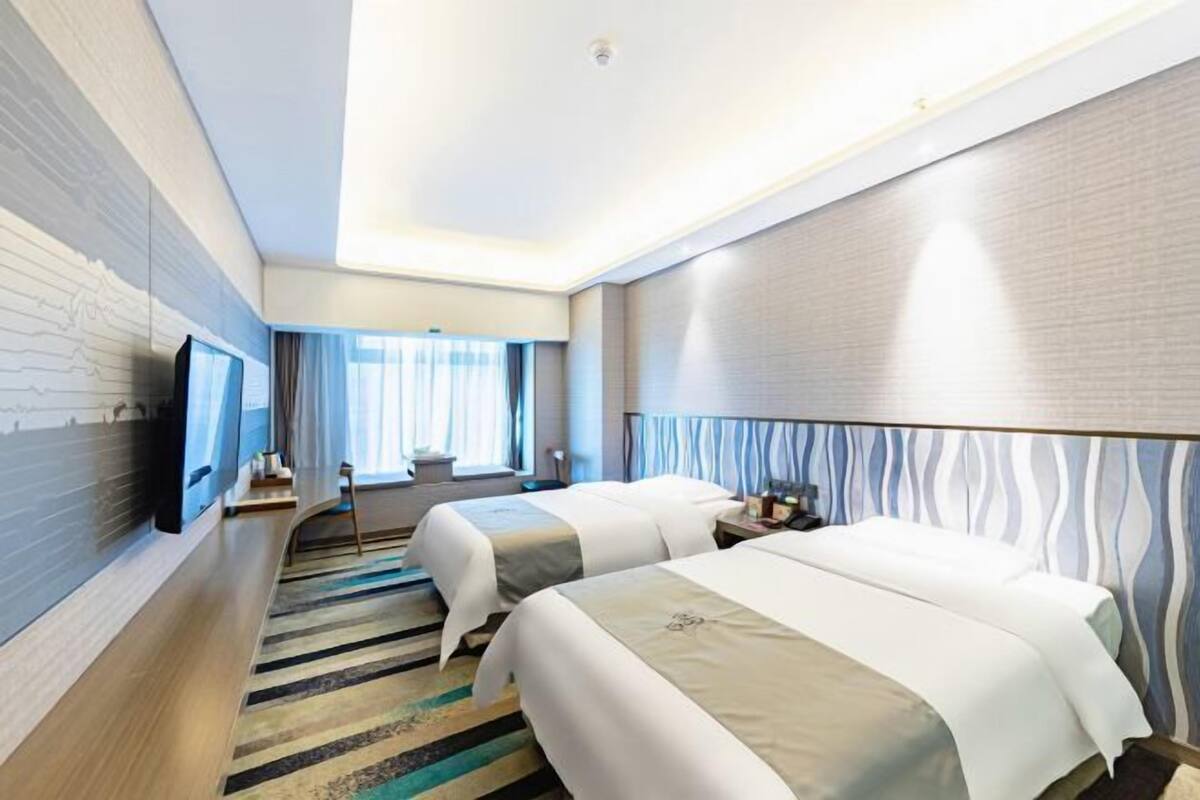 Una habitación de hotel con dos camas, un televisor de pantalla plana, un ventanal con cortinas y una alfombra estampada.