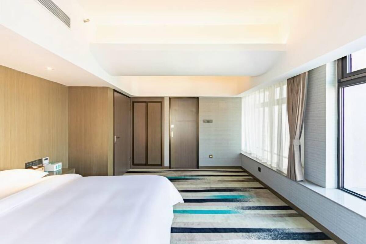 Una habitación de hotel con una cama, una mesita de noche, una ventana con cortinas y una puerta.