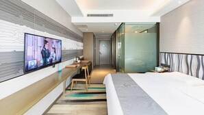 Una habitación de hotel moderna con televisor, escritorio, cama y un separador de vidrio.