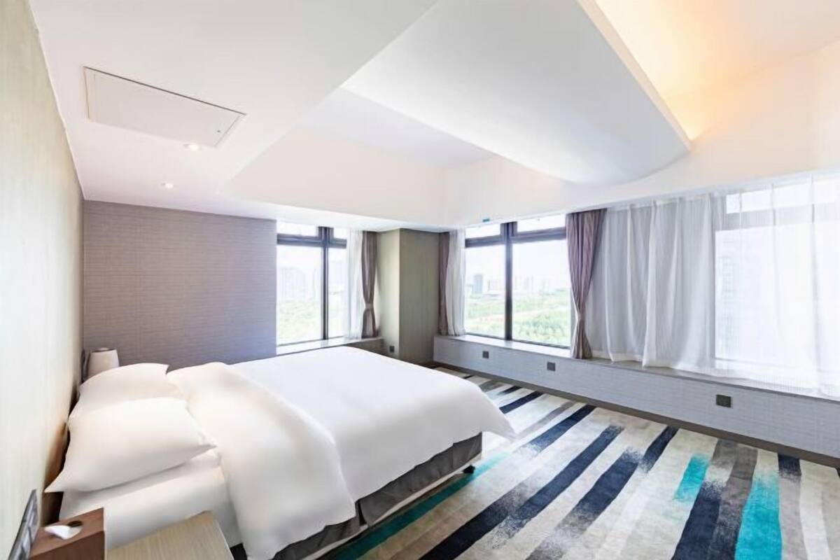 Una habitación de hotel moderna con una cama grande, una ventana con cortinas y una alfombra a rayas.