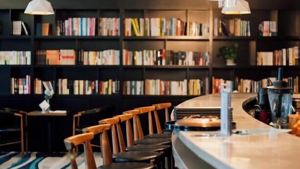 Una zona de bar con sillas de madera y una barra, rodeada de estanterías llenas de libros.