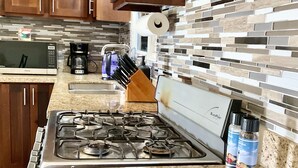 A kitchen with wooden cabinets, a gas stove, a microwave, and a tiled backsplash.