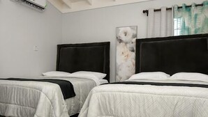 A hotel room with two beds, a large window with curtains, and a wall-mounted air conditioner.