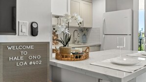 A modern kitchen with white cabinets, a marble countertop, a wicker basket with a candle, and a welcome sign. -  NO PARKING & RESORT FEE IN WEST MAUI WITH AMAZING OCEAN VIEW CONDO (Lahaina)