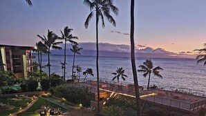 A swimming pool surrounded by lounge chairs and palm trees, with a view of the ocean and a building in the background. -  NO PARKING & RESORT FEE IN WEST MAUI WITH AMAZING OCEAN VIEW CONDO (Lahaina)