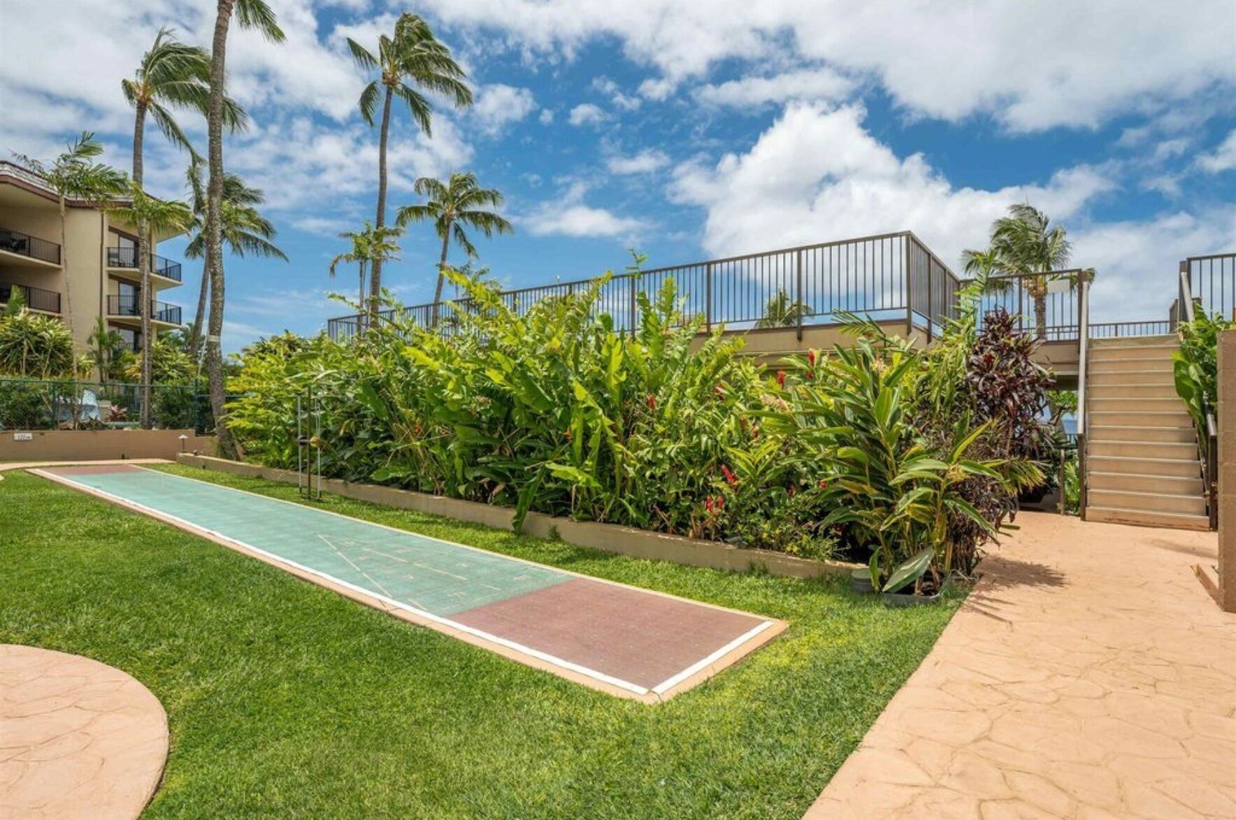 A well-maintained outdoor area with a green tennis court, palm trees, and a building with balconies.