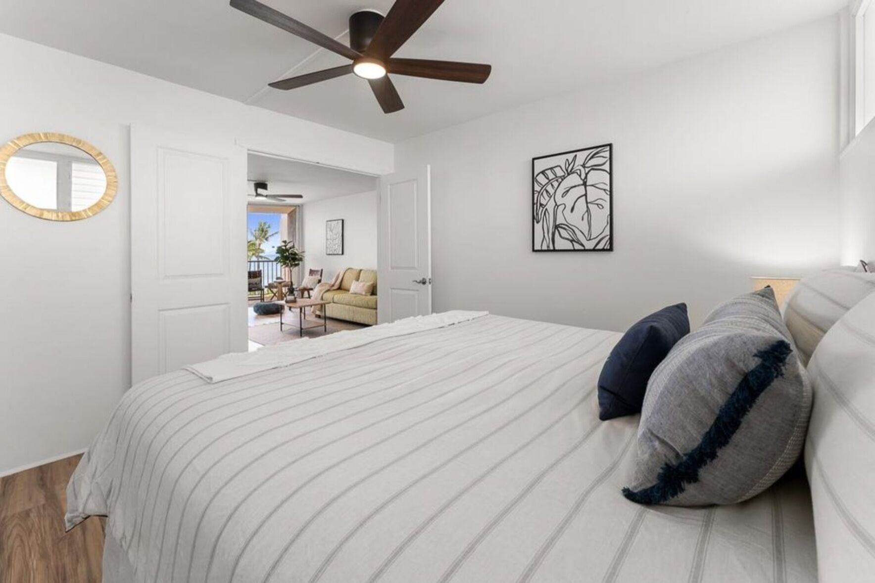 Een slaapkamer met een bed, een plafondventilator, een spiegel aan de muur en een deur naar een andere kamer.