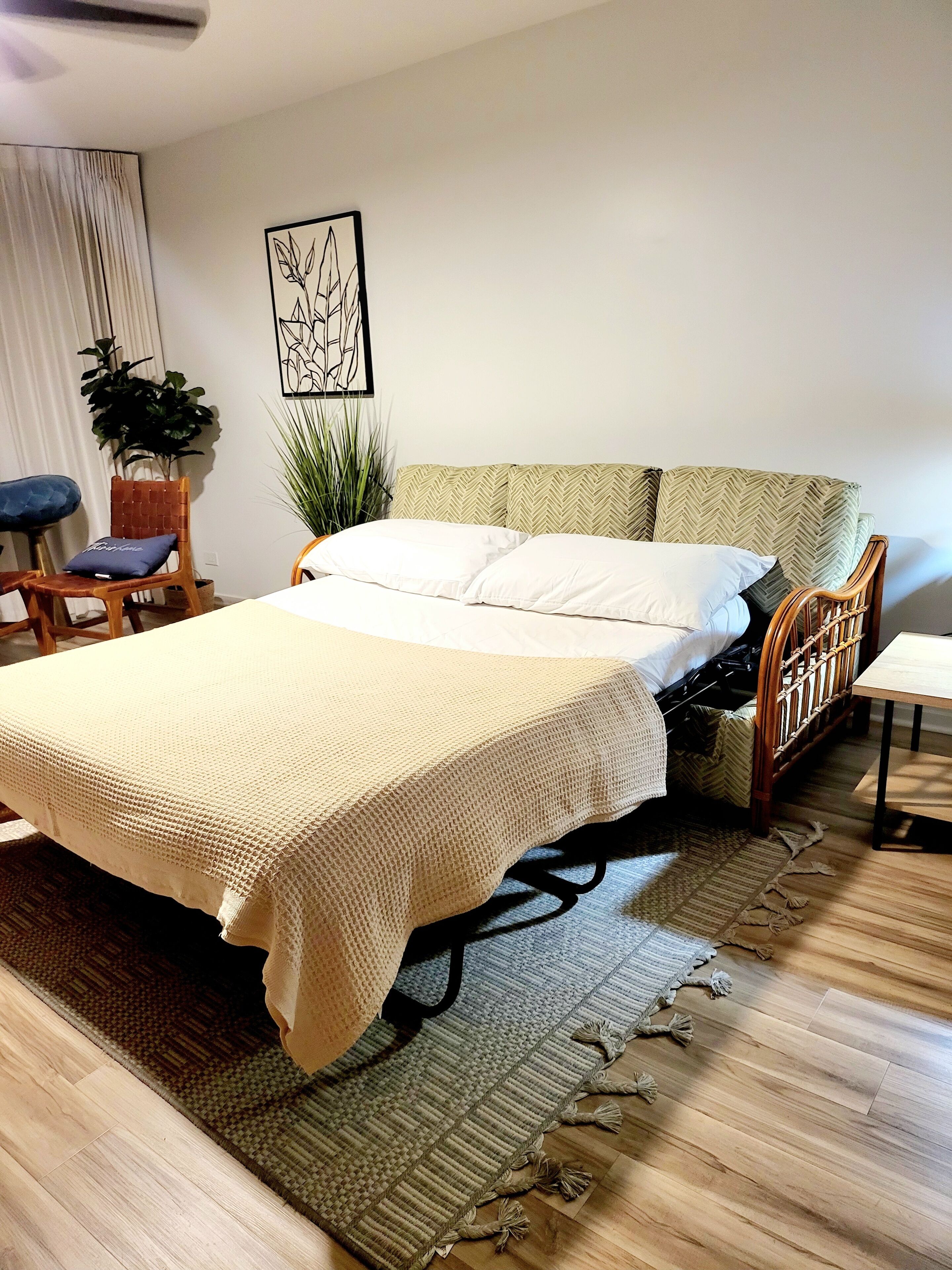 Un dormitorio ordenado con una cama, una silla, una mesita y una planta en maceta.