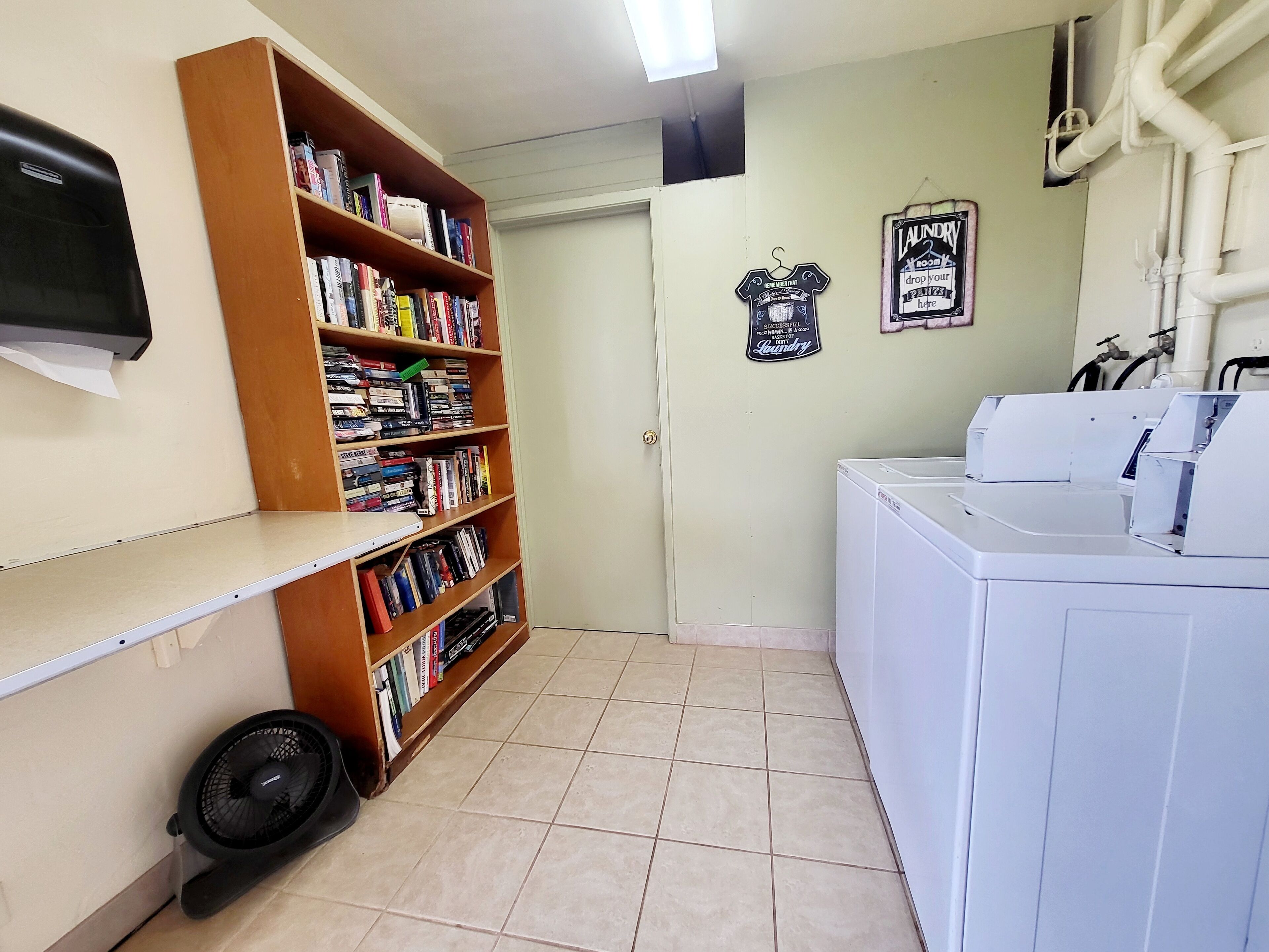 Un angolo lavanderia con lavatrice, una ventola e una libreria piena di libri.