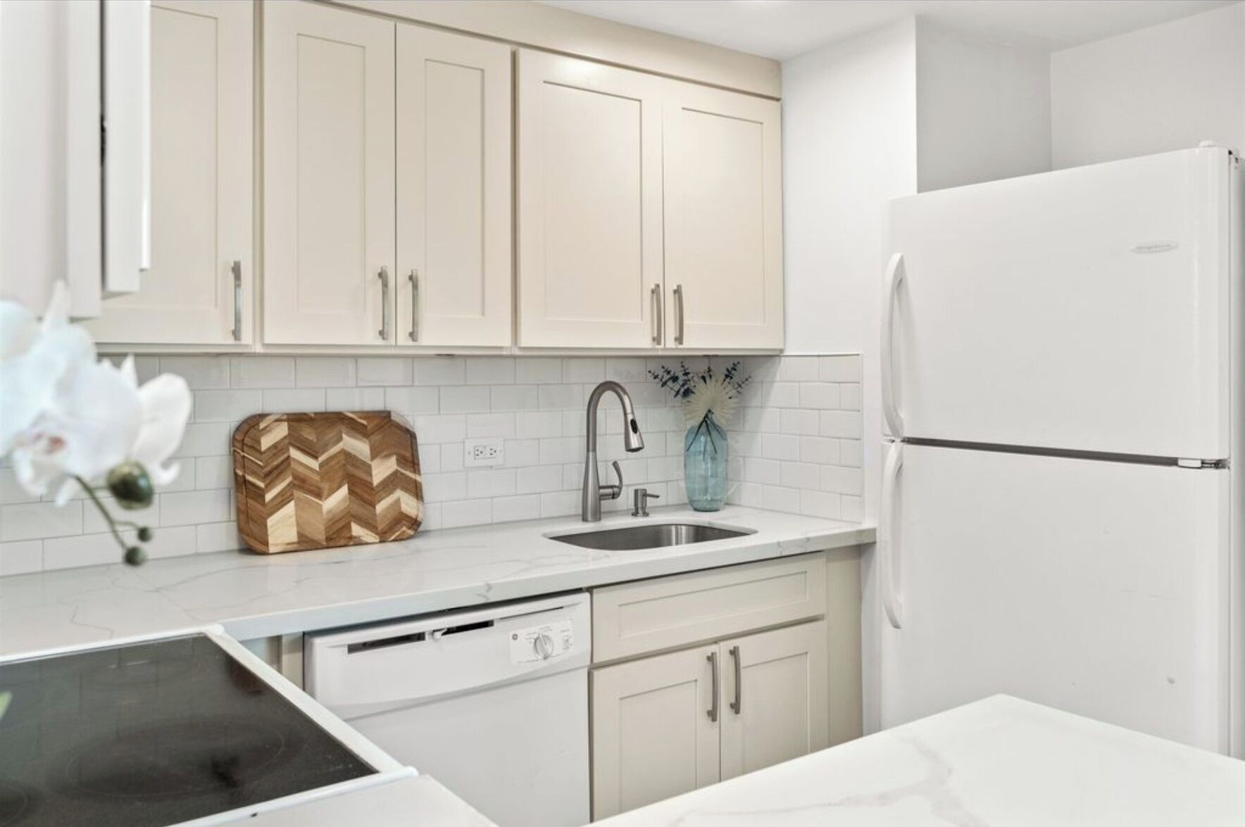 A modern kitchen with white cabinetry, a stainless steel sink, a dishwasher, and a white refrigerator.