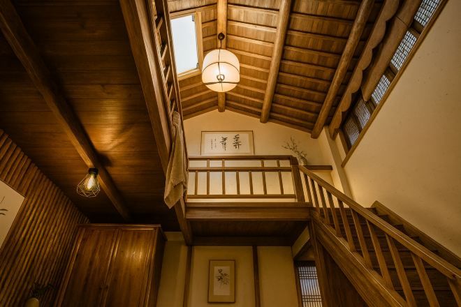 Interior de madeira com escada, luminária pendente e quadro na parede.