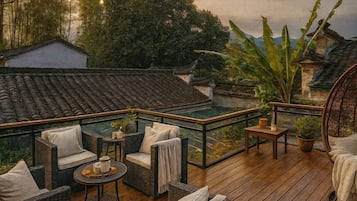 Een houten terras met rieten meubilair, een klein tafeltje en een potplant.
