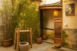 A traditional Japanese-style courtyard with a wooden bench, potted plants, and a tiled roof.