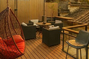 Una terraza de madera con mobiliario exterior, que incluye una silla colgante, sofás y una mesa.