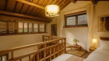 Quarto com teto de madeira, uma cama, mesa de cabeceira, abajur, janela com cortinas e uma pequena mesa com uma planta.
