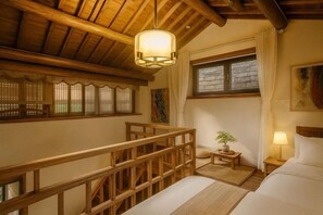 Una habitación con techo de madera, una cama, una mesita de noche, una lámpara, un ventanal con cortinas y una pequeña mesa con una planta.