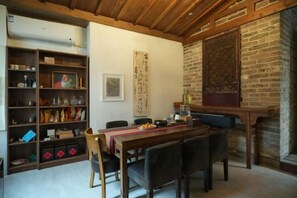 A dining area with a long table, chairs, a bookshelf, and a fireplace. - Xidi Zhuguangli · Mindful Aesthetic Homestay (Yi County)