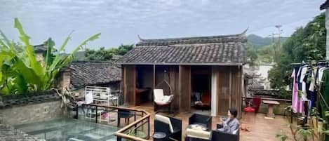 Un edificio de estilo tradicional con una terraza de madera, una piscina con fondo de cristal y vistas del paisaje circundante.