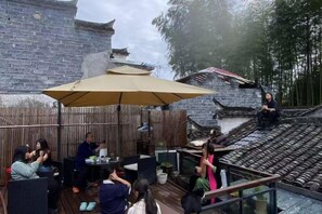 An outdoor seating area with tables and chairs, a large umbrella, and a view of a traditional building. - Xidi Zhuguangli · Mindful Aesthetic Homestay (Yi County)