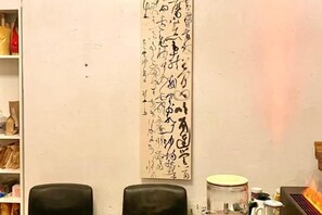 Una habitación con una obra de arte alargada sobre la pared, dos sillas negras y una pequeña mesa con un tarro y un recipiente.