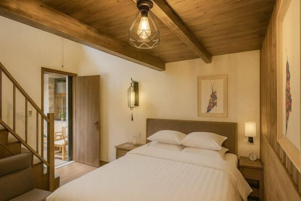 Une chambre avec un plafond en bois, un lit recouvert de linge de lit blanc, une table de chevet avec une lampe et un tableau accroché au mur.