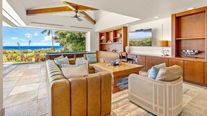 Tilava olohuone, jossa on suuri sohva, ruokapöytä ja näkymä merelle.