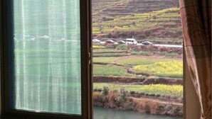 Une fenêtre donnant sur des champs en terrasses et sur un véhicule au loin.