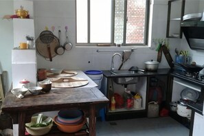 A kitchen with a wooden table, various cooking utensils, a sink, and a window with a view of a brick wall. - He'an Renjia Farm Stay (Wuyuan)