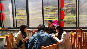 A group of people dining at a table with a view of terraced fields through large windows.