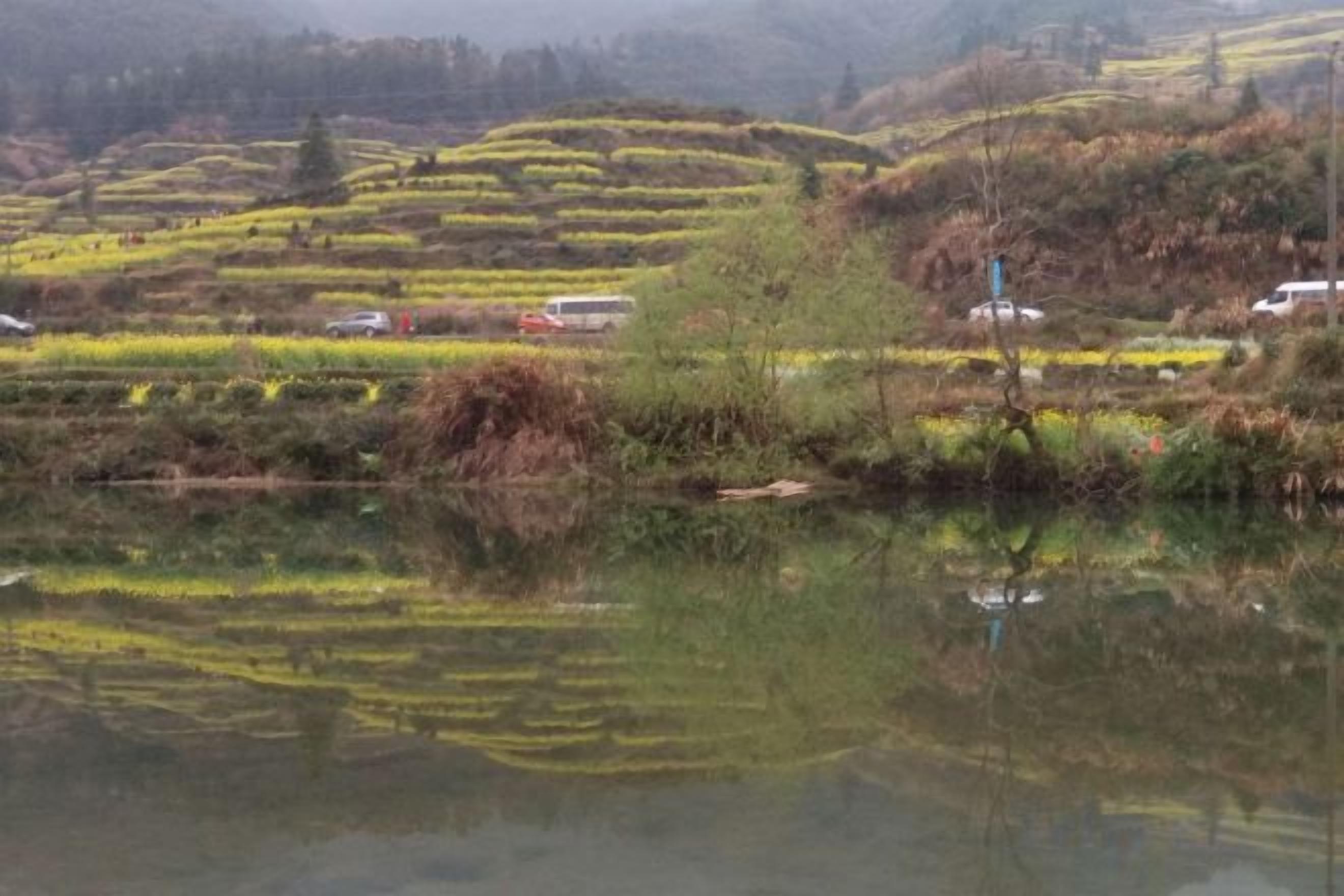 A serene landscape with terraced fields and a calm body of water reflecting the surroundings.